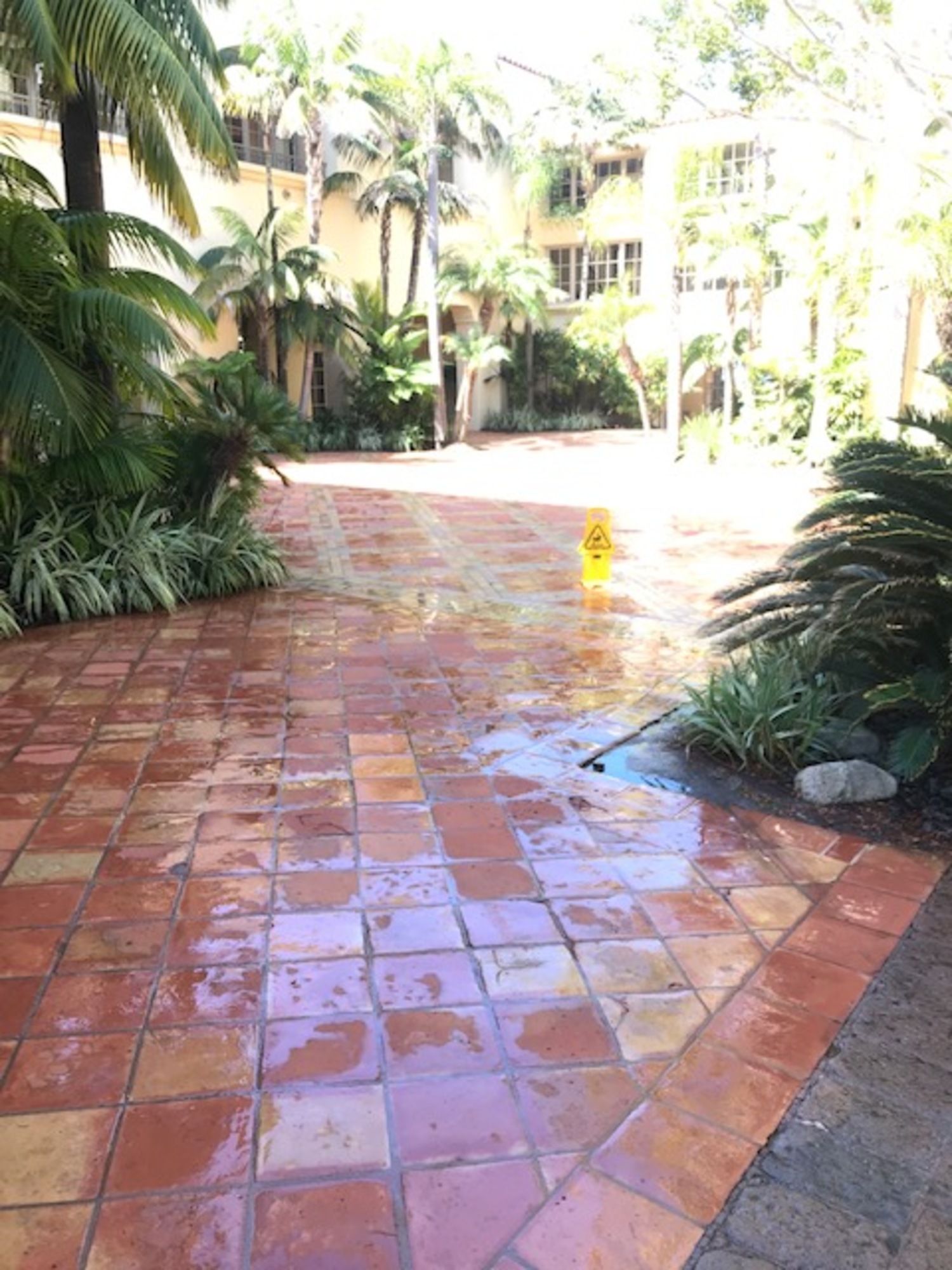 A brick walkway with a yellow wet floor sign in the middle of it.