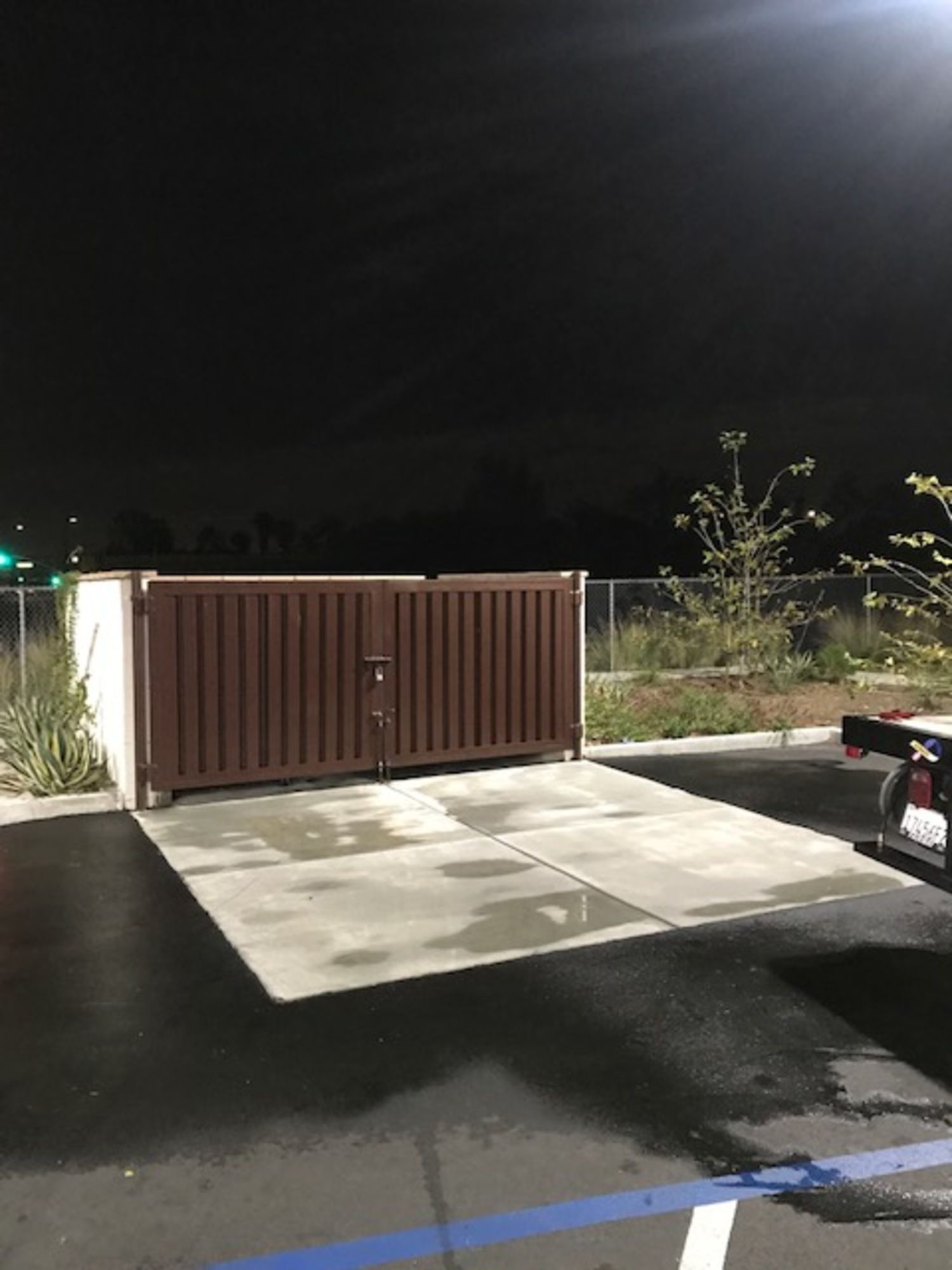 A car is parked in a parking lot next to a fence at night.