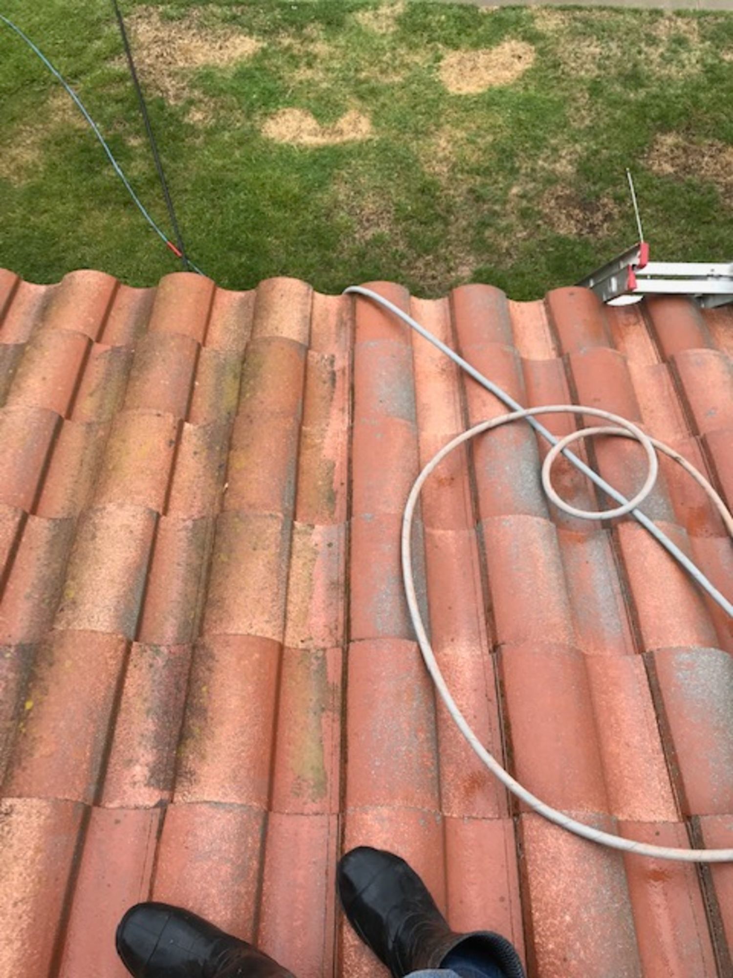 A person is laying on top of a tiled roof with a hose attached to it.
