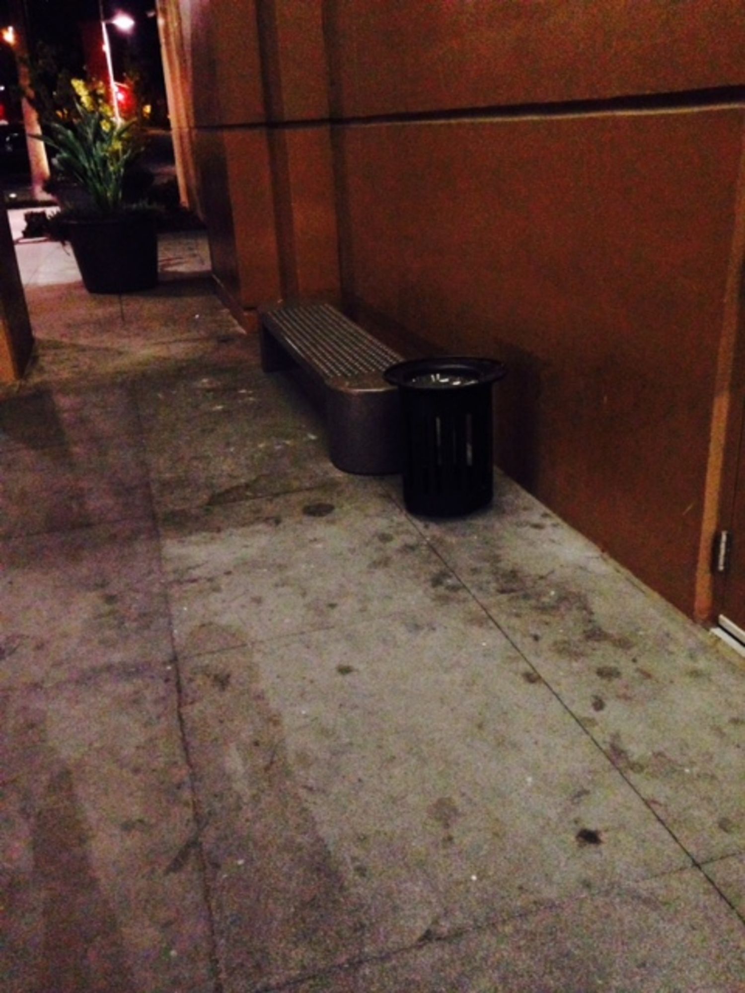 A dirty sidewalk with a bench and a trash can