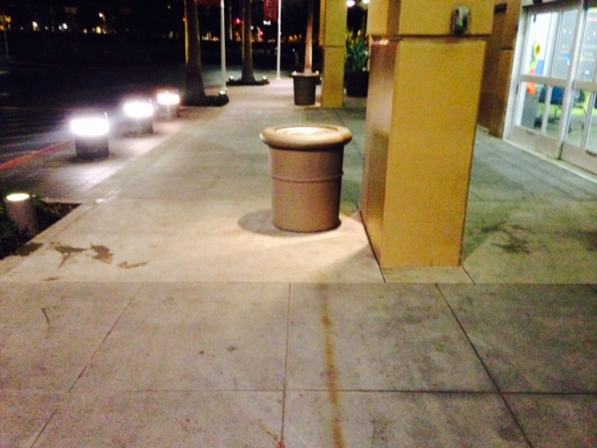 A trash can sits on a sidewalk in front of a building