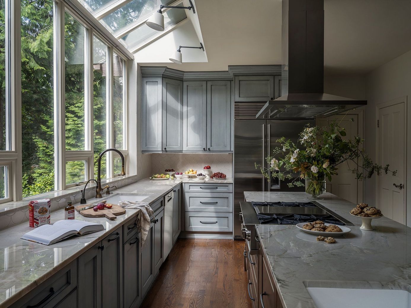 Kitchen with blue cabinets, stainless steel appliances, and large windows overlooking trees.