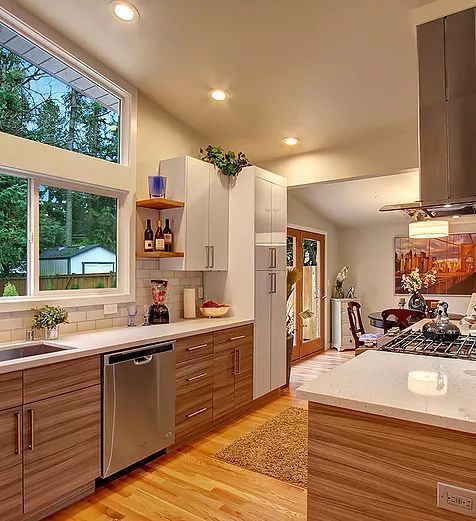 Modern kitchen with wooden cabinets, stainless steel appliances, and large window overlooking a yard.