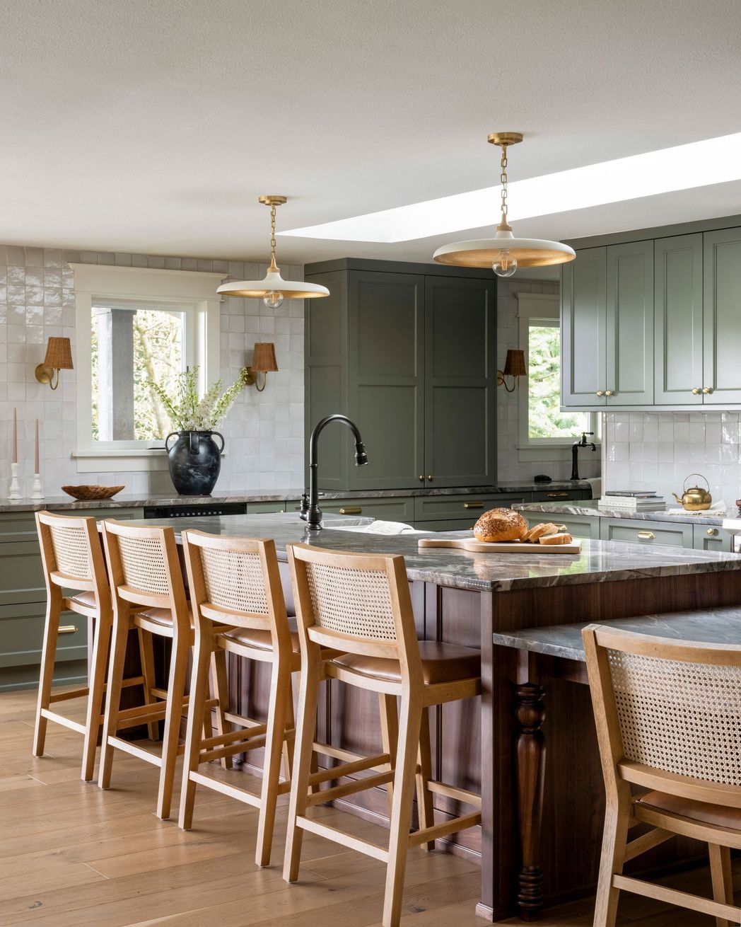 Kitchen with sage green cabinets, dark island, and light wood bar stools.