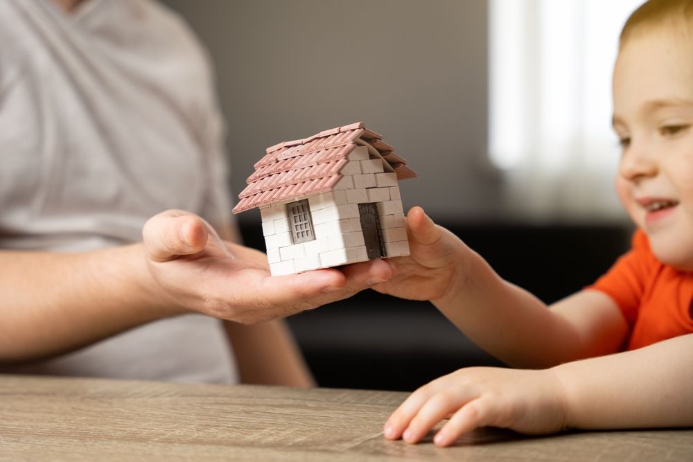 A person and a child hold a small model house together.