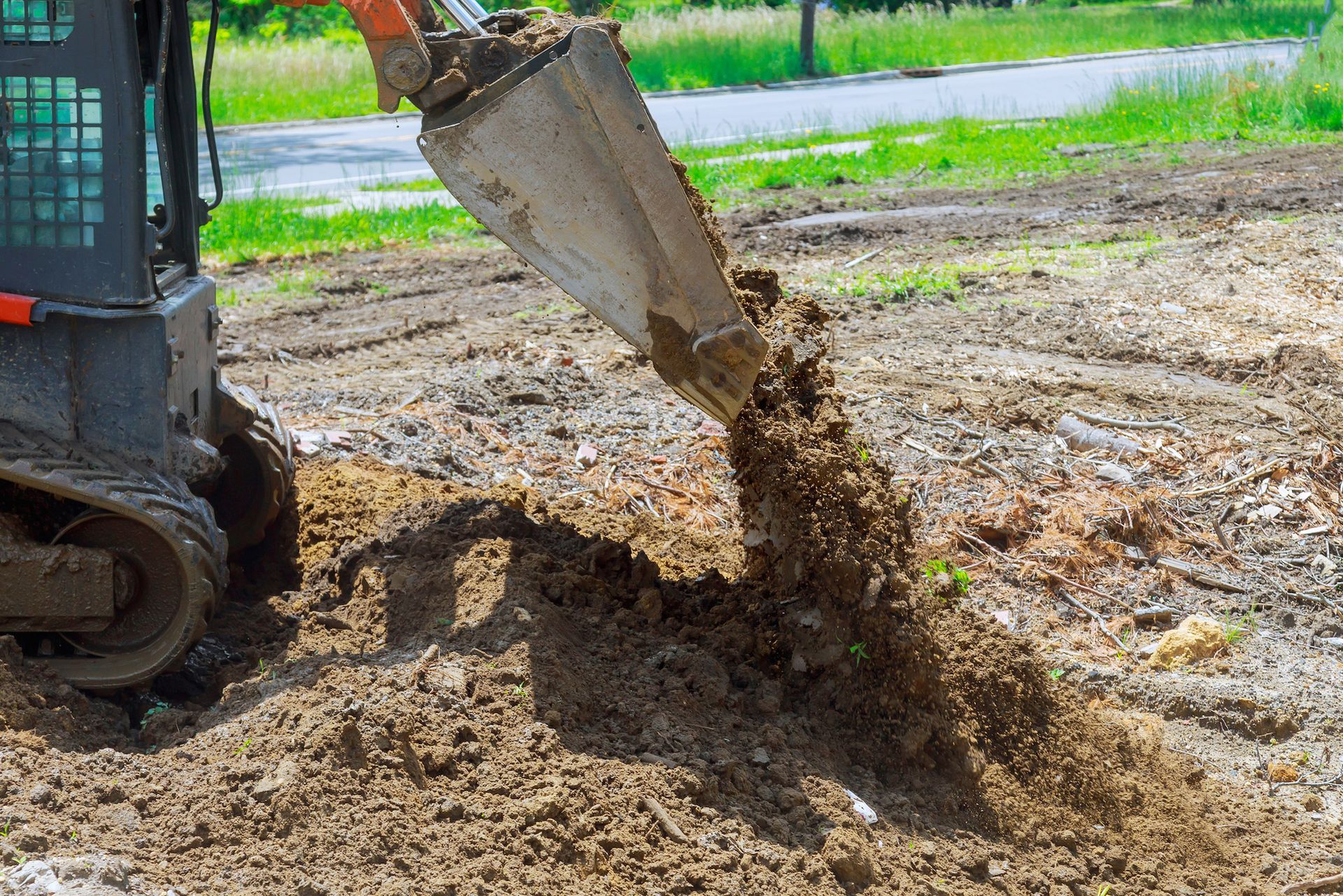 Excavator bucket dumping wet soil onto a muddy construction site