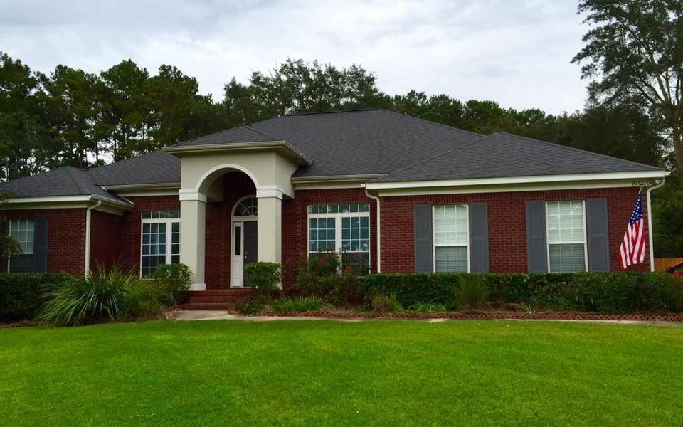 Single-story red brick house with white columns, gray roof, and a green lawn