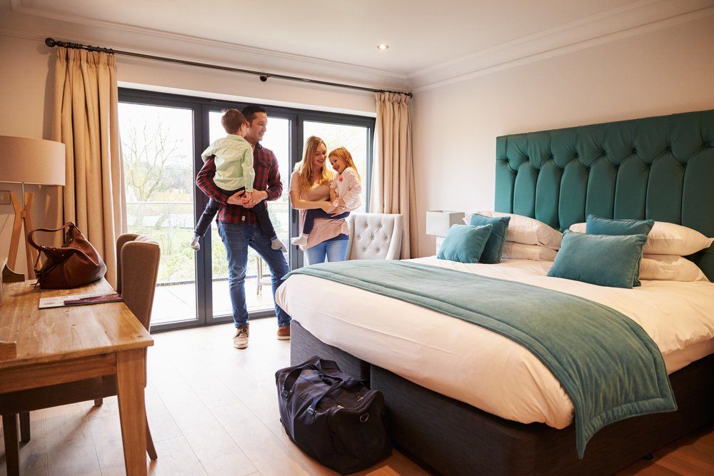 Family with young children entering a modern hotel room with a large bed, luggage, and natural light