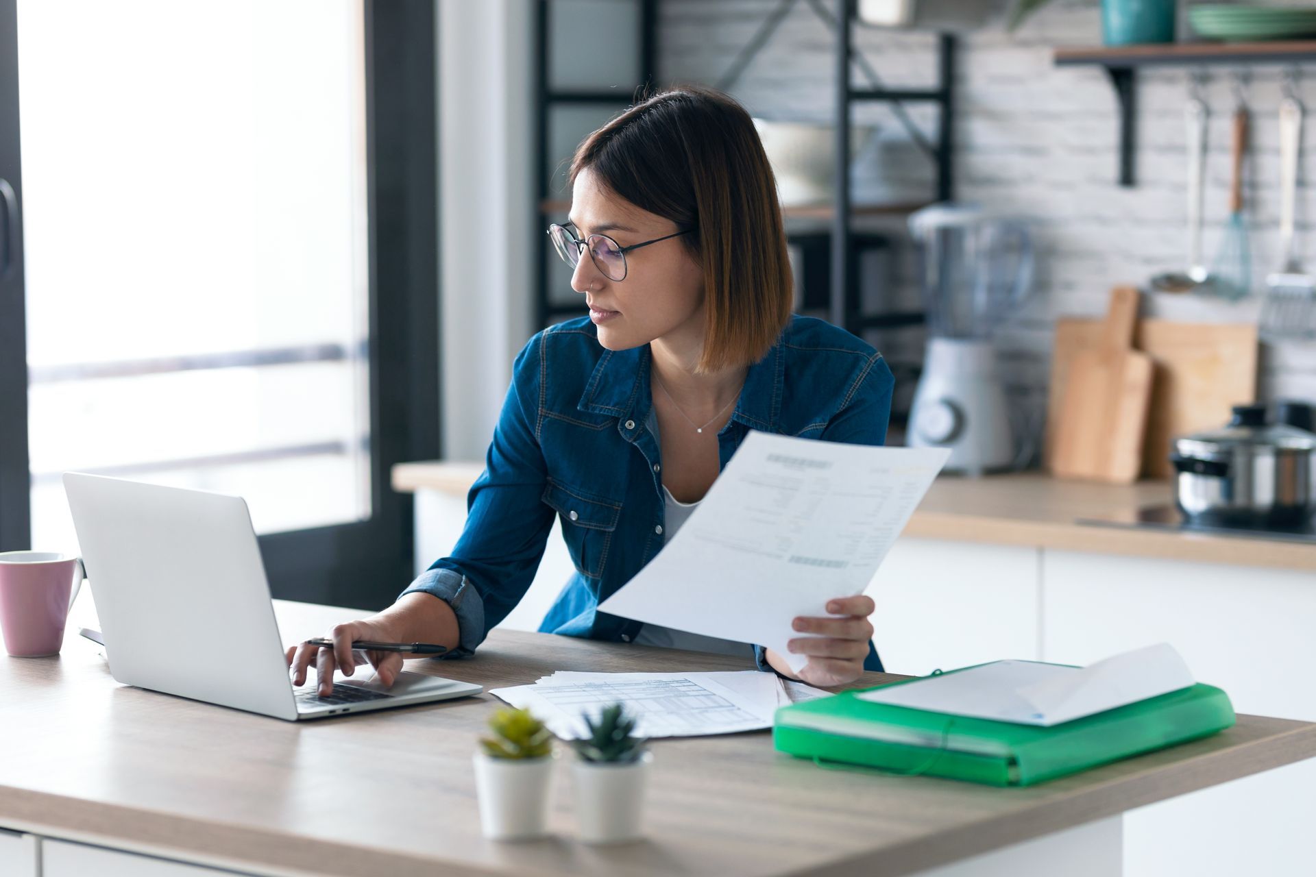 Une femme est assise en utilisant un ordinateur portable et en tenant un morceau de papier.