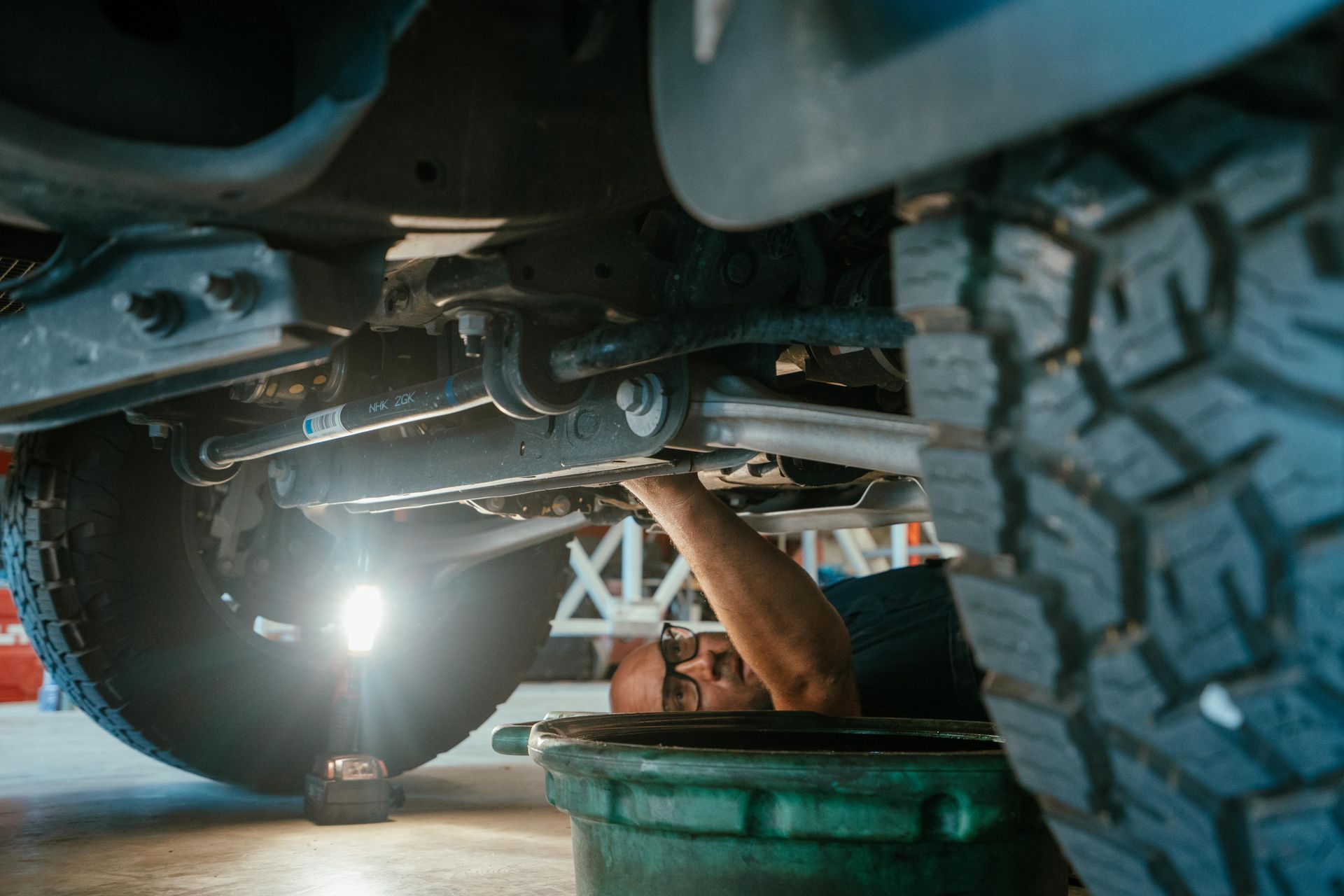 Mechanic working under a vehicle, changing oil, illuminated by a light. Oil pan below the car. — Navan Mobile Mechanic in Dapto, NSW