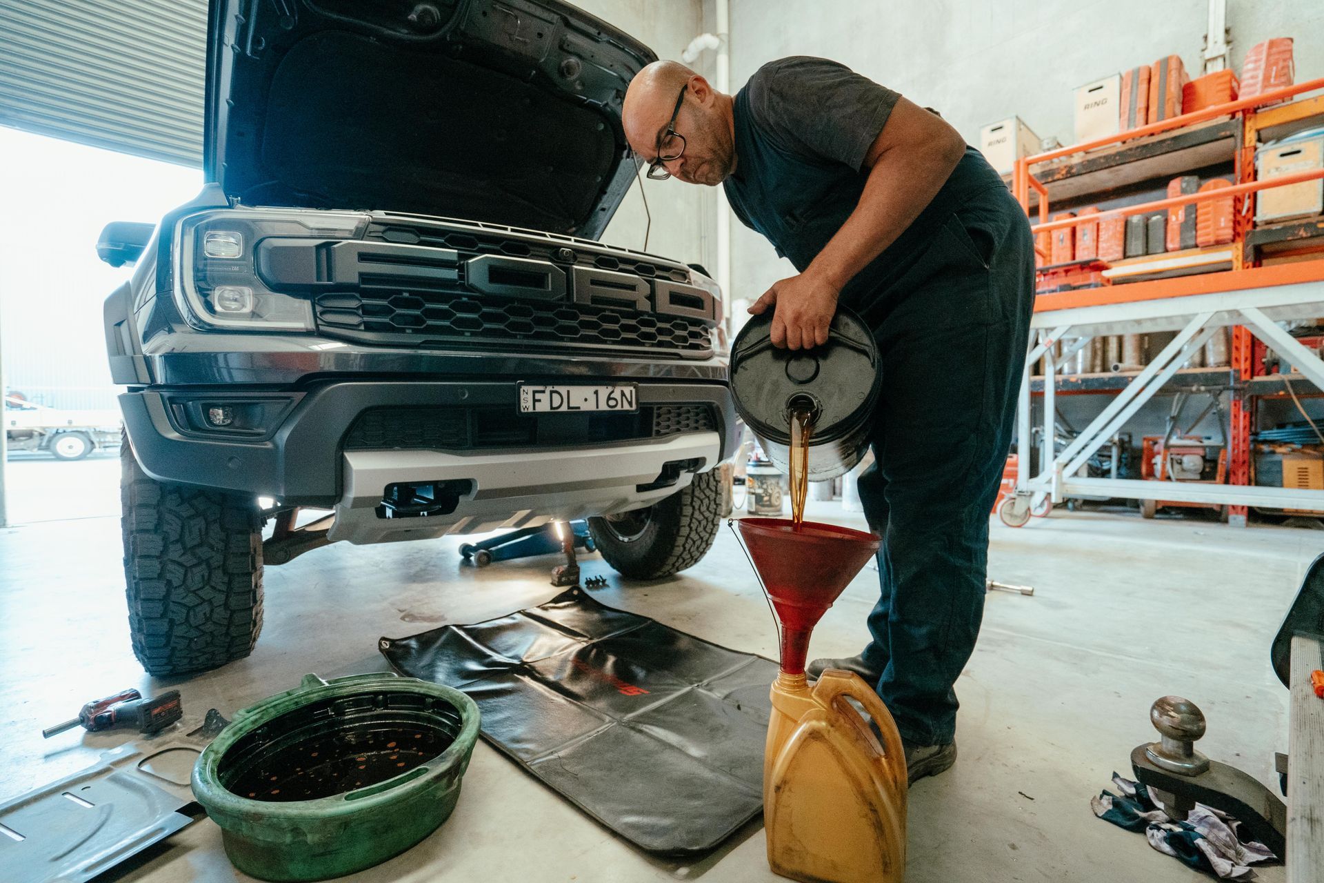 Mechanic pouring oil into a car engine, changing oil in a garage.