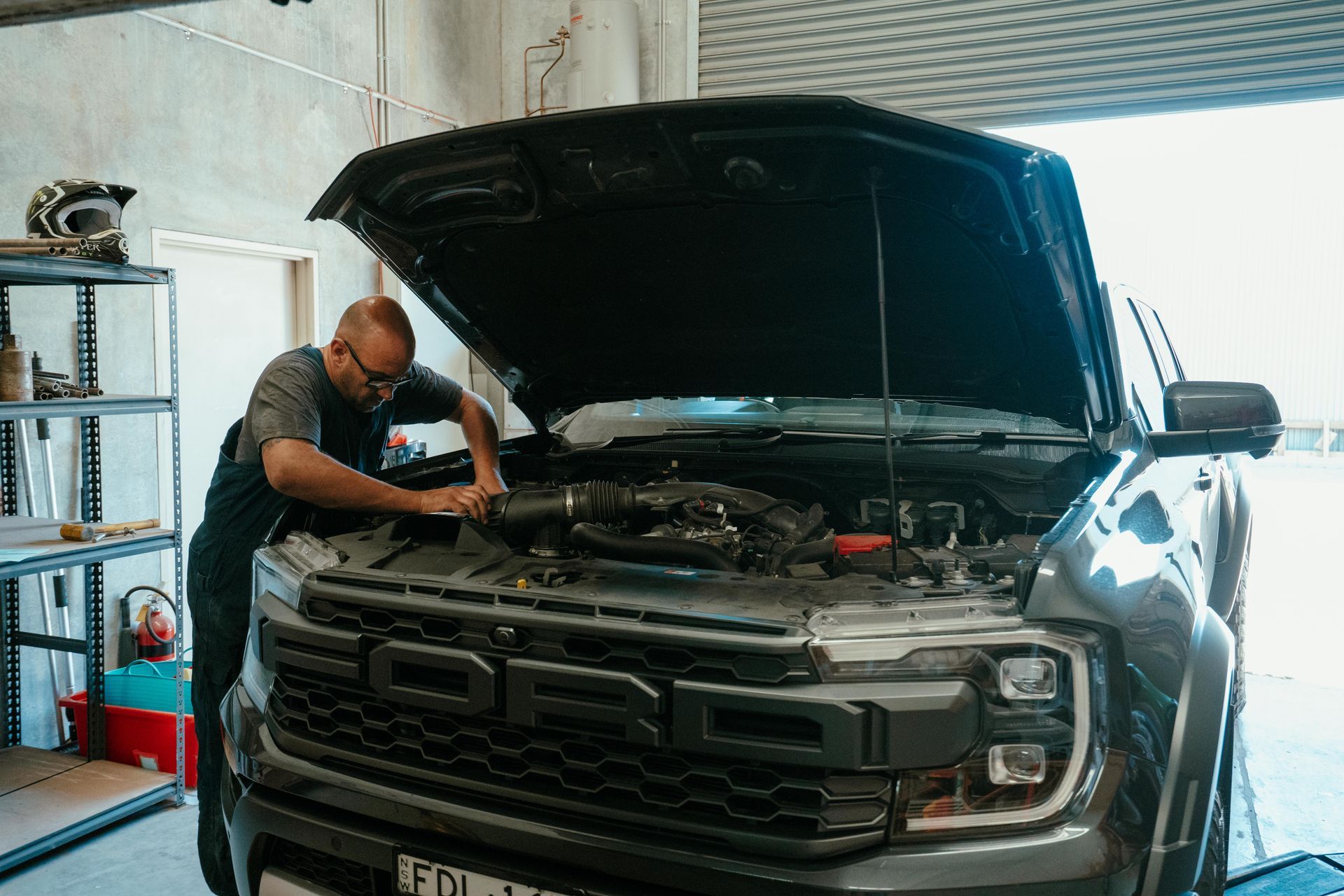 Mechanic working on the engine of a black Ford Raptor truck with the hood open in a garage. — Navan Mobile Mechanic in Corrimal, NSW