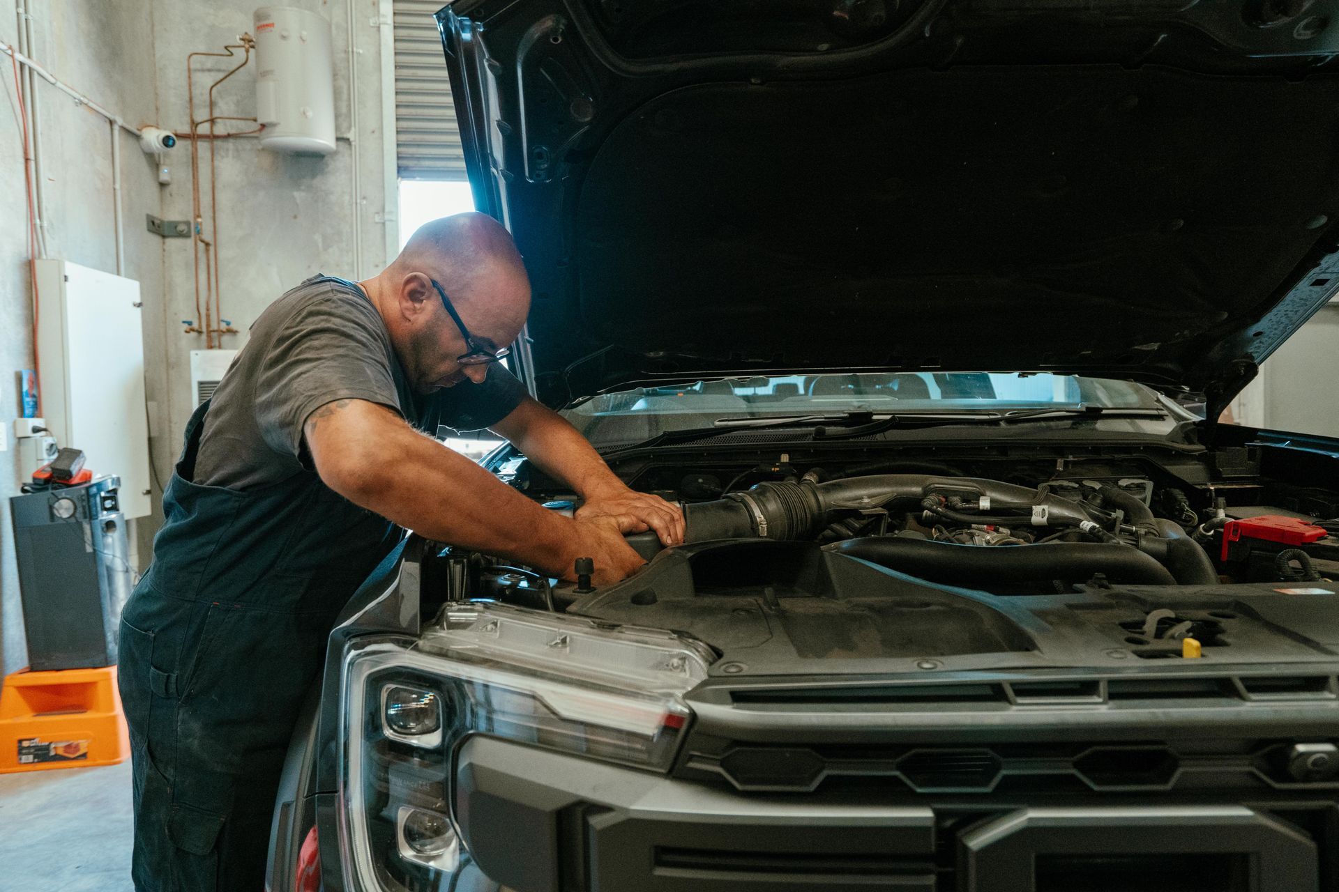 Mechanic working on a black car engine with the hood open in a garage — Navan Mobile Mechanic in Corrimal, NSW