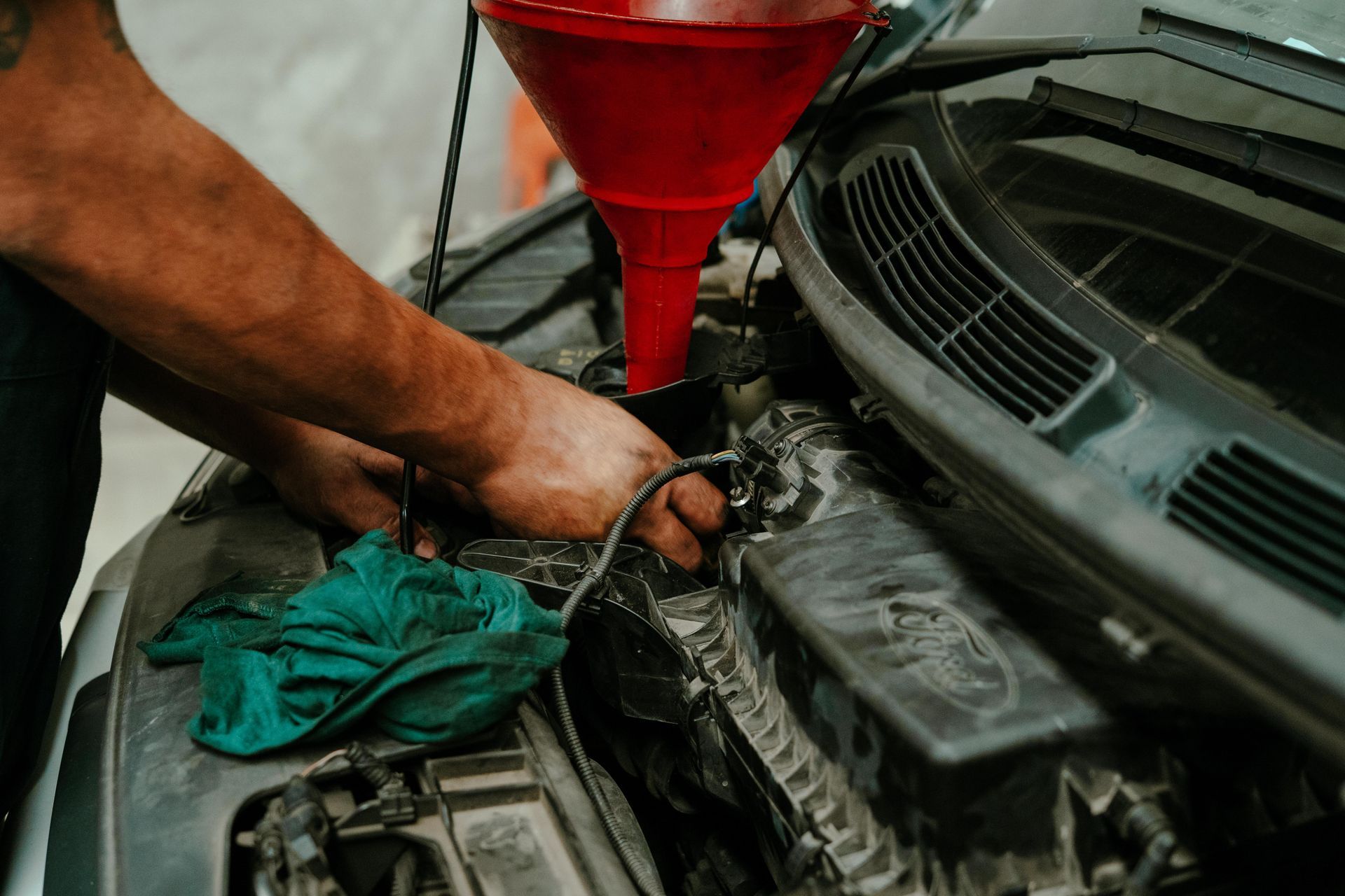 Hands of a person working on a car engine, using a red funnel to pour a liquid. — Navan Mobile Mechanic in Albion Park, NSW