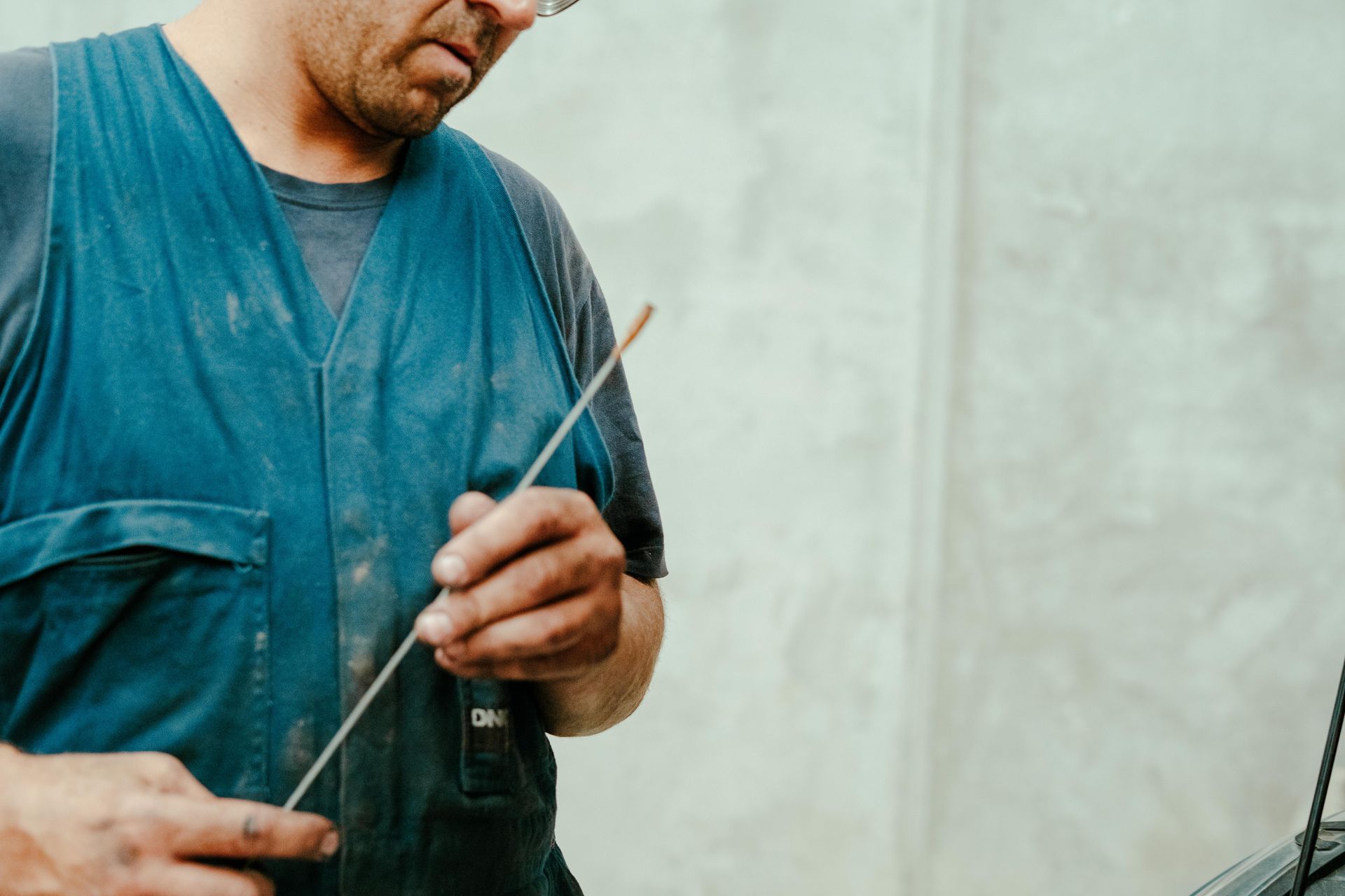 Man holding a thin metal rod, wearing a blue vest, standing in a workshop. — Navan Mobile Mechanic in Dapto, NSW