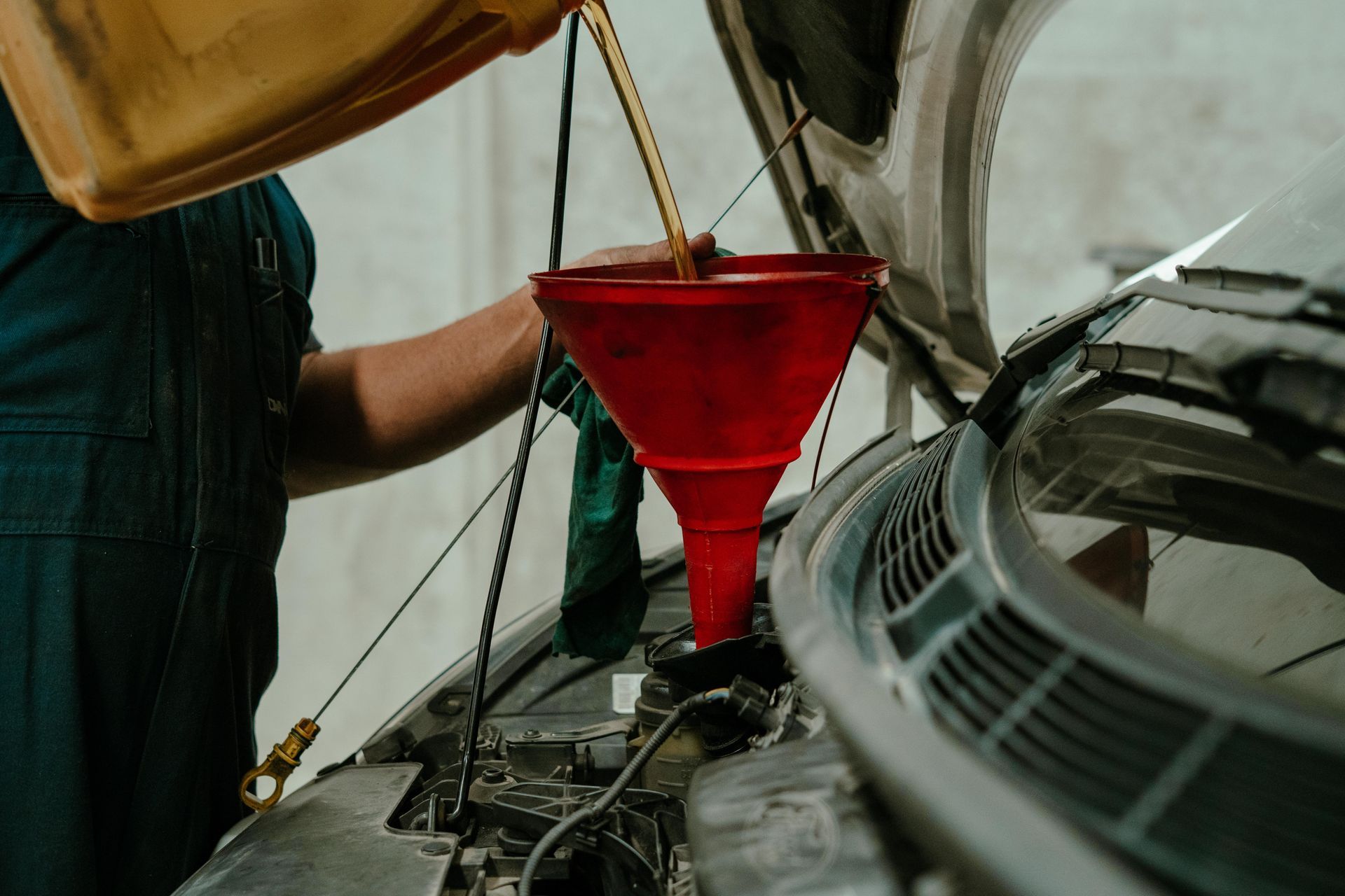 Mechanic pouring oil into a car engine using a red funnel in a garage — Navan Mobile Mechanic in Corrimal, NSW