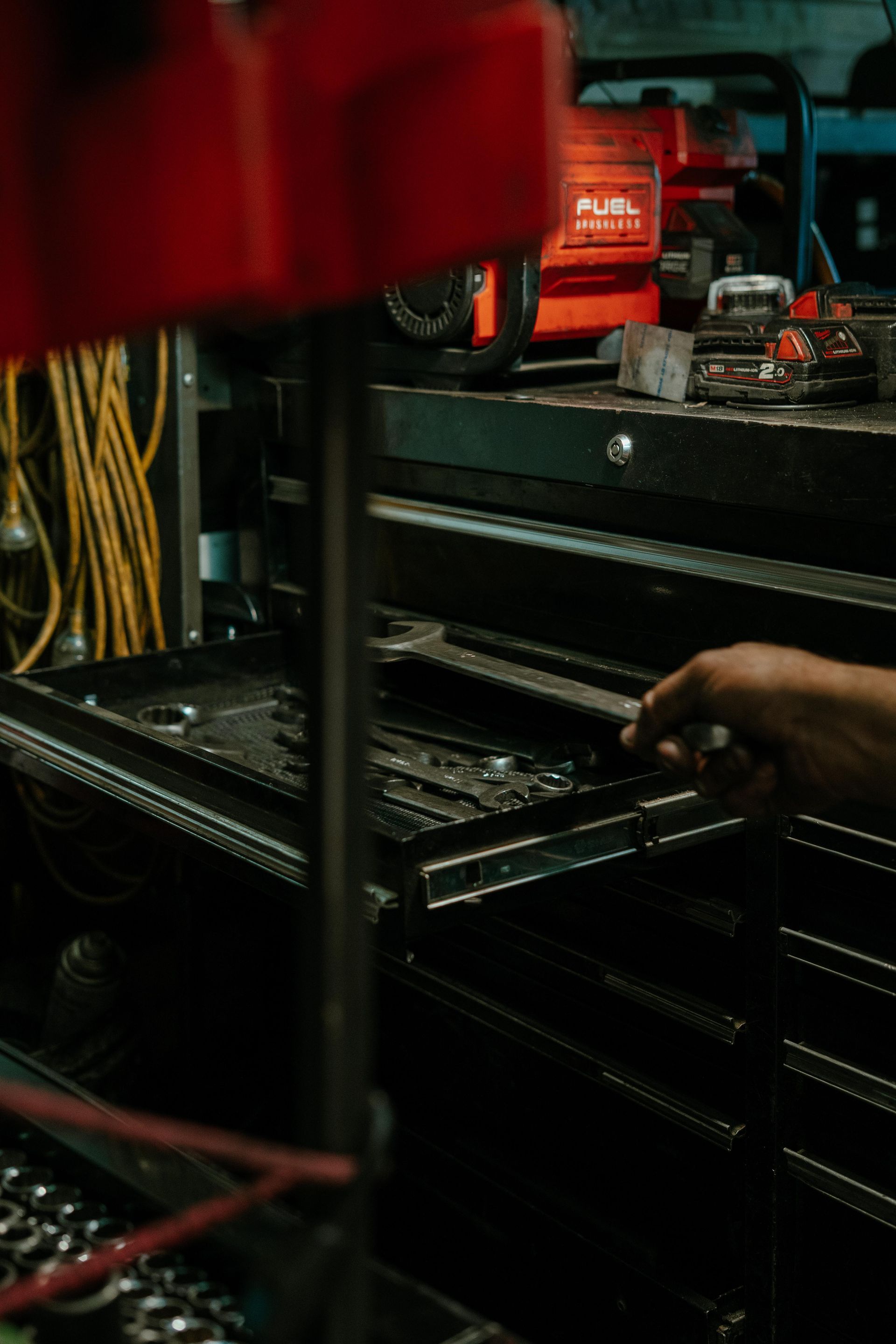 Person's hand reaching into a black toolbox, possibly for a wrench. Orange tool and red object visible in background. — Navan Mobile Mechanic in Unanderra, NSW