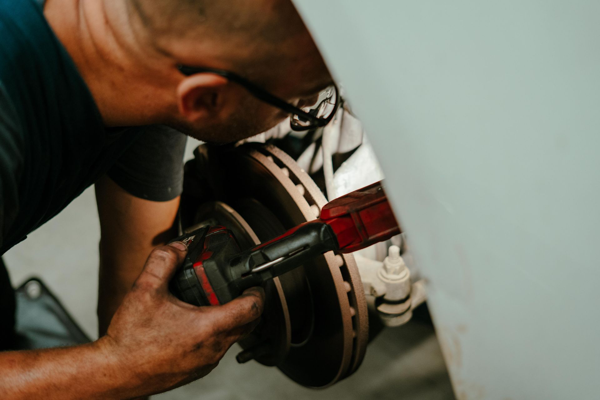 Mechanic using a power tool on a car's brake rotor, outdoors. — Navan Mobile Mechanic in Shellharbour, NSW