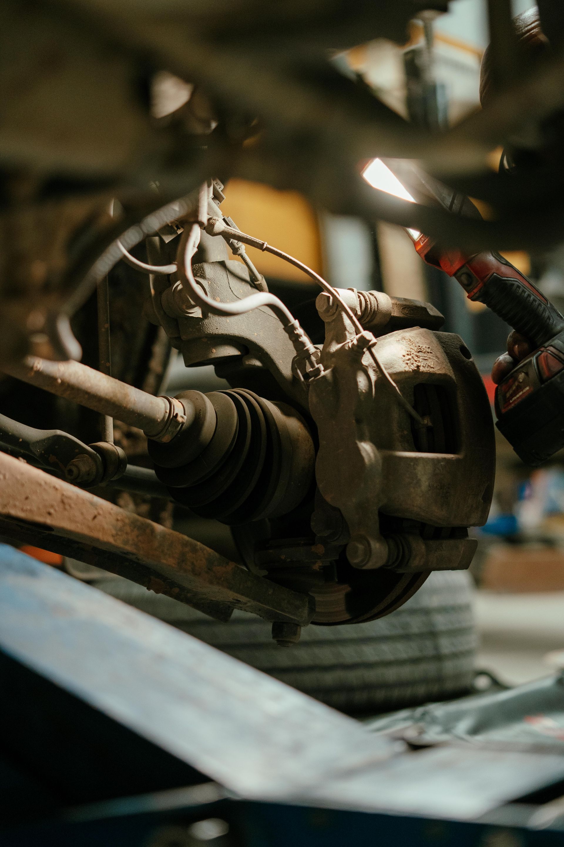 Car brake assembly being inspected, illuminated by a flashlight in a dimly lit garage. — Navan Mobile Mechanic in Albion Park, NSW
