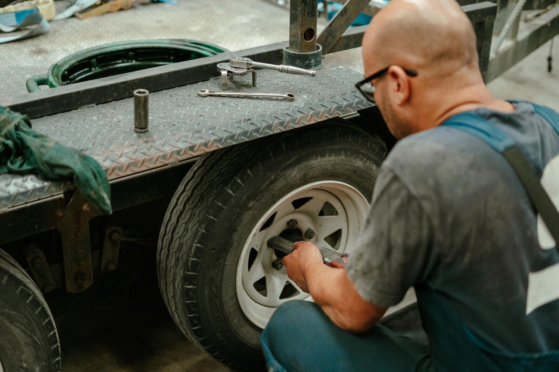 Man working on a trailer tyre with tools on the trailer's metal surface; indoor setting. — Navan Mobile Mechanic in Corrimal, NSW