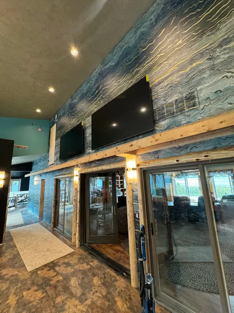 A wall with blue-and-gold textured wallpaper featuring two mounted televisions above glass patio doors and wooden posts.