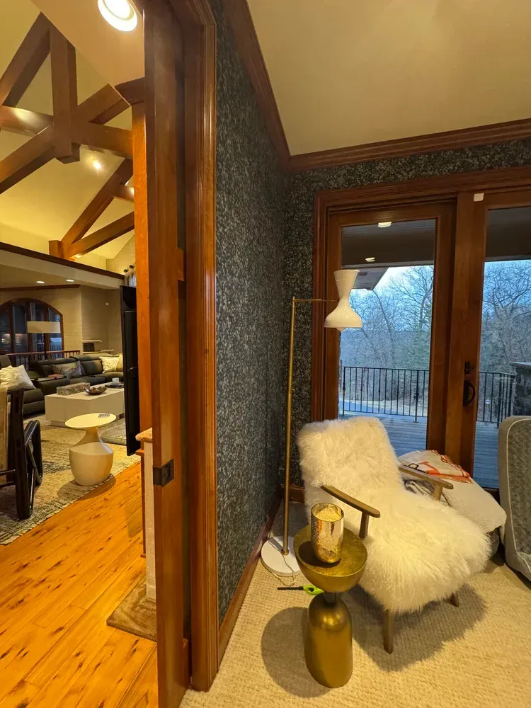 A cozy reading nook featuring a white faux-fur armchair, a gold pedestal side table, and a floor lamp against dark wallpaper.