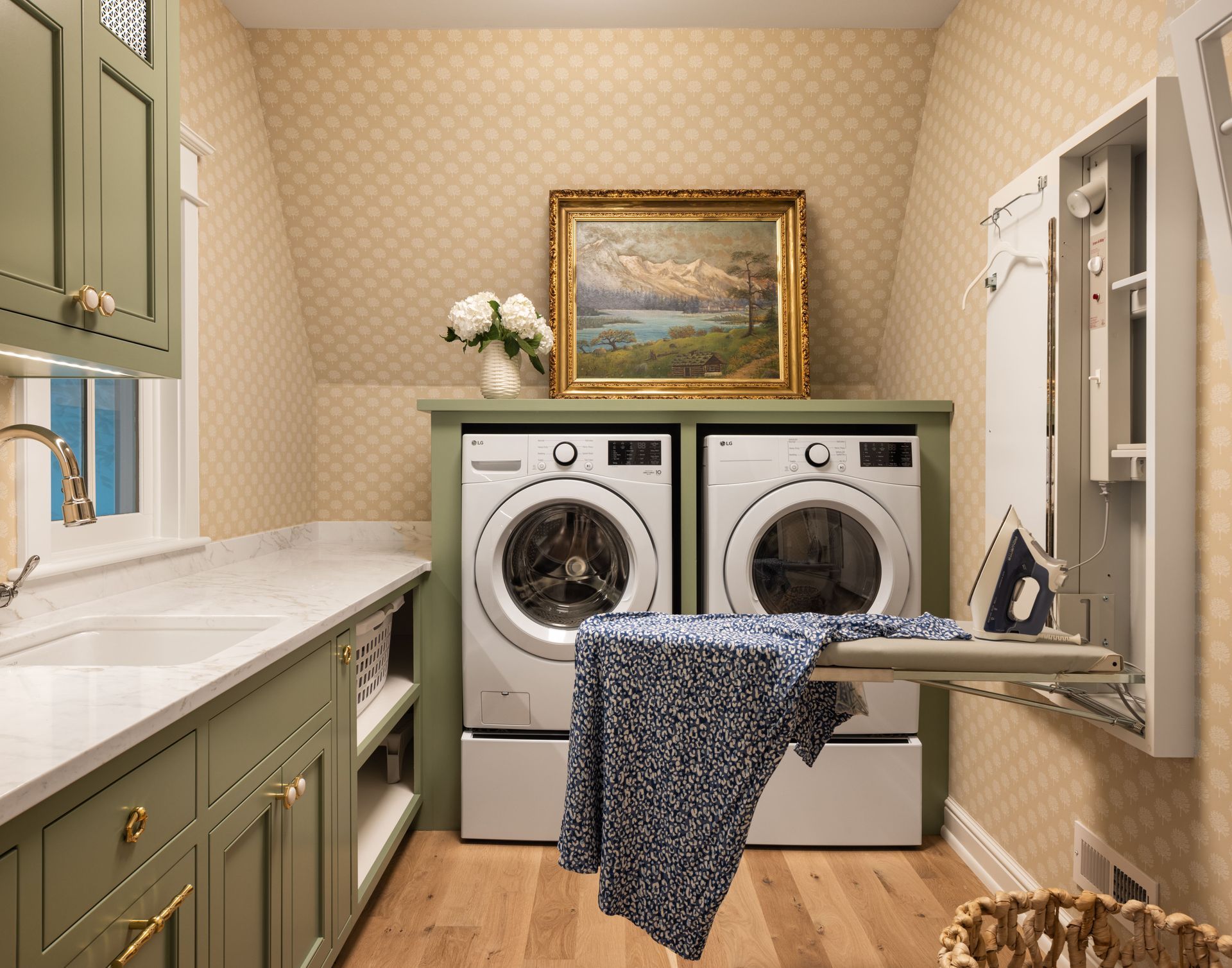 A laundry room with sage green cabinets, white countertops, a washer, a dryer, and a wall-mounted fold-out ironing board.