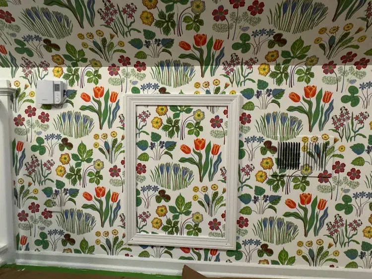 A wall covered in floral wallpaper with tulips and clover motifs, featuring a central white rectangular frame.