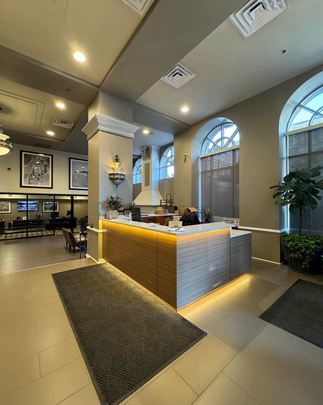 Modern hotel lobby with a reception desk, gray floor mats, and arched windows under recessed lighting.