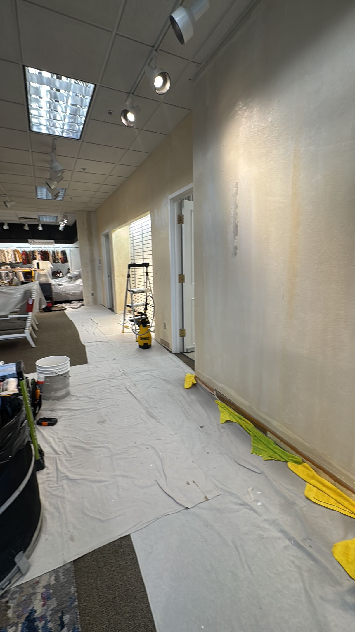 An interior view of a room under renovation, with protective floor coverings, a ladder in the distance, and bare walls.