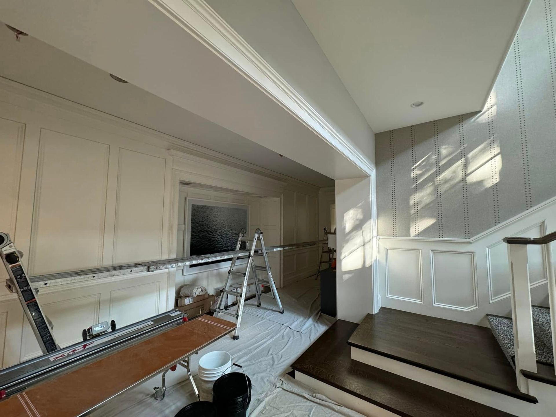 A home interior under construction with a ladder, painting equipment, and scaffolding in a room with a staircase.