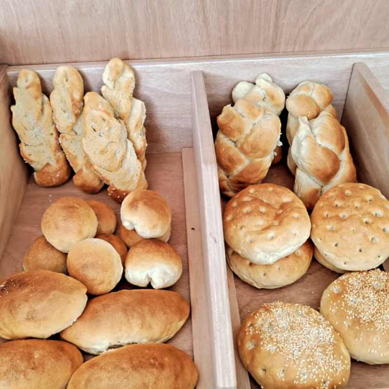 Espositore per il pane in scomparti di legno; varie forme, tra cui panini, trecce e pagnotte.