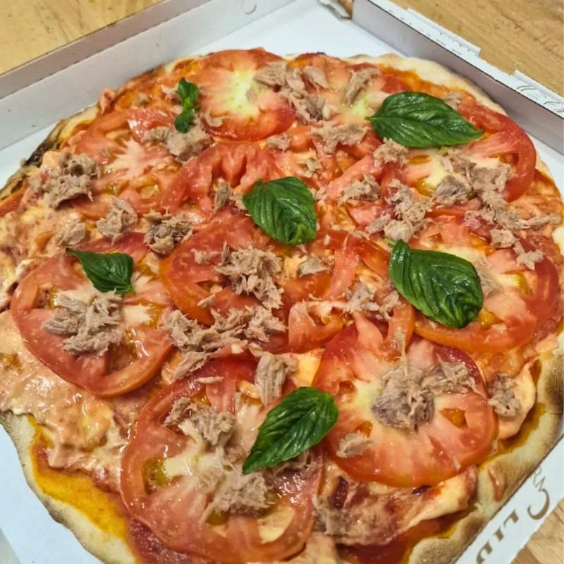 Pizza con pomodori, tonno e basilico, in una scatola di cartone.
