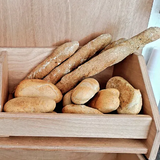 Cestino del pane pieno di vari panini e grissini in un contenitore di legno.