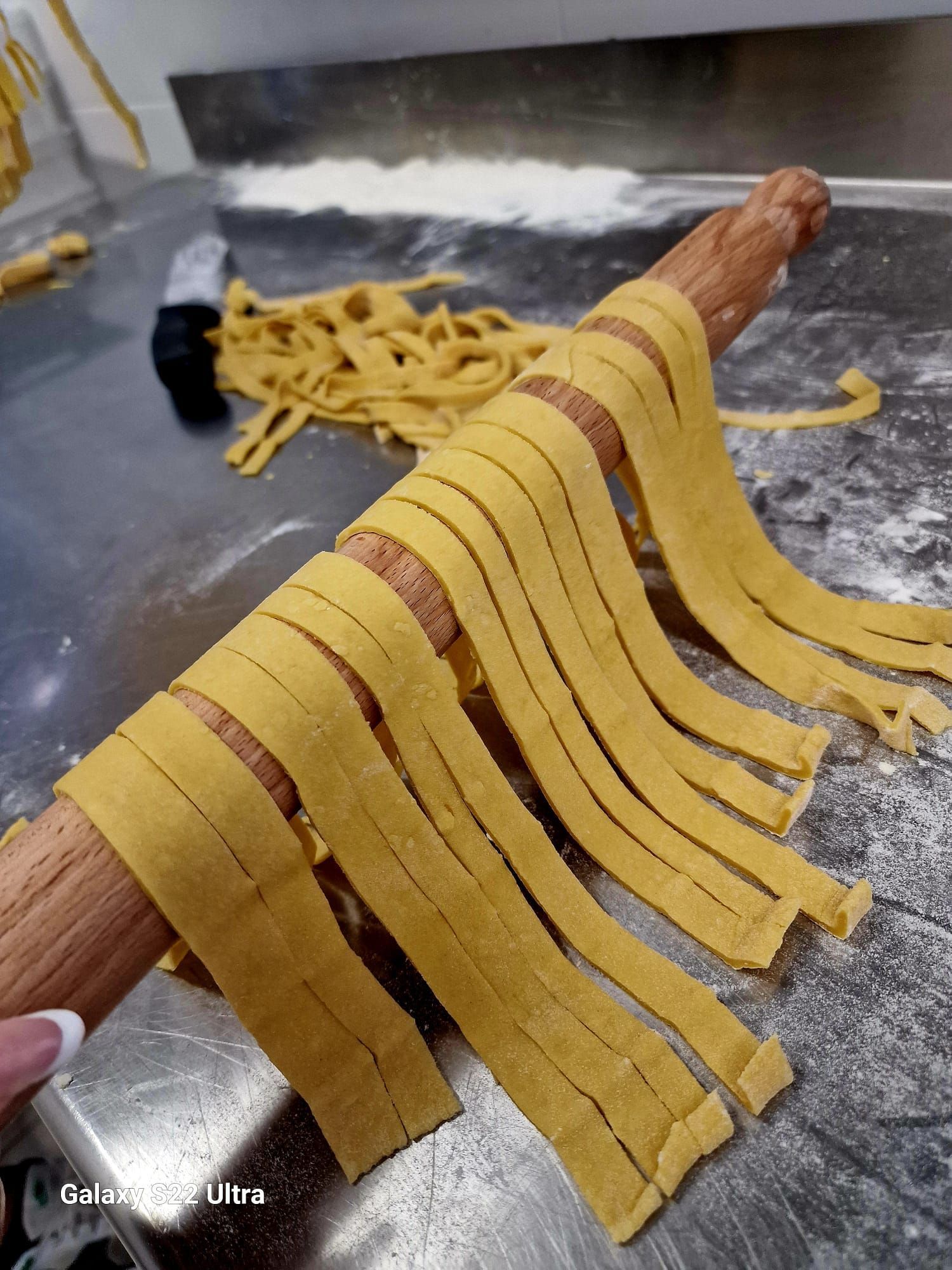 Nastri di pasta fresca stesi su un mattarello e appoggiati su una superficie metallica infarinata.