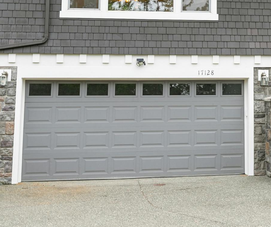 Gray double garage door repaired on a house exterior with white trim and stone siding, house number 1728 above it