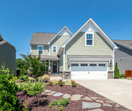 Suburban two-story beige house with white garage, stone landscaping, and a bright blue sky