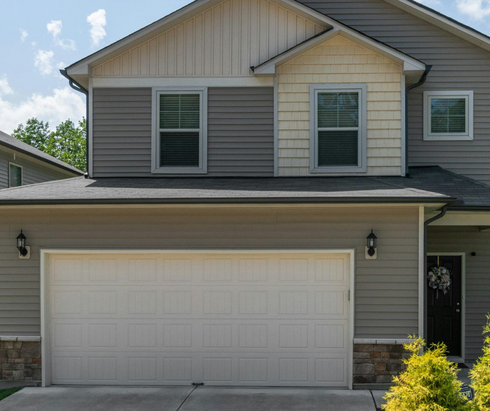 Suburban two-story gray house with a white garage door and black front entrance under a gabled roof.