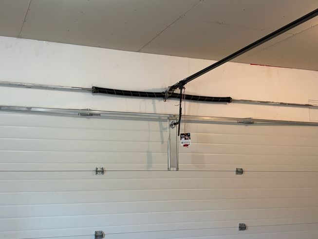 Garage door opener track and hardware mounted above a white sectional garage door repair.