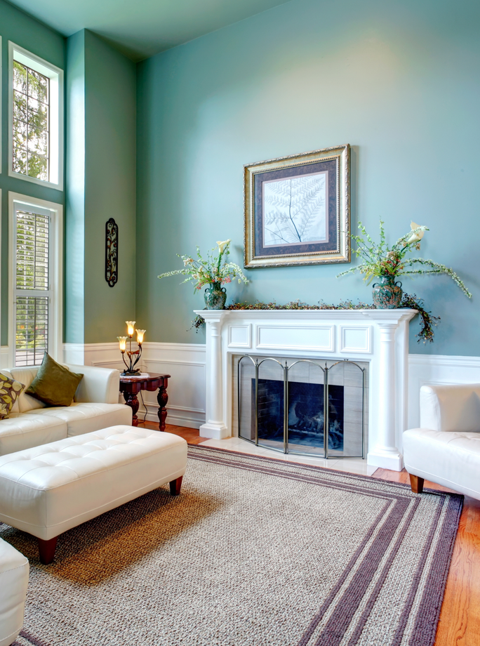 A living room with blue walls , white furniture , a fireplace and a rug.