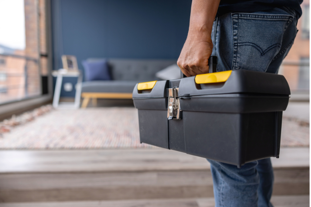 A man is carrying a toolbox in a living room.