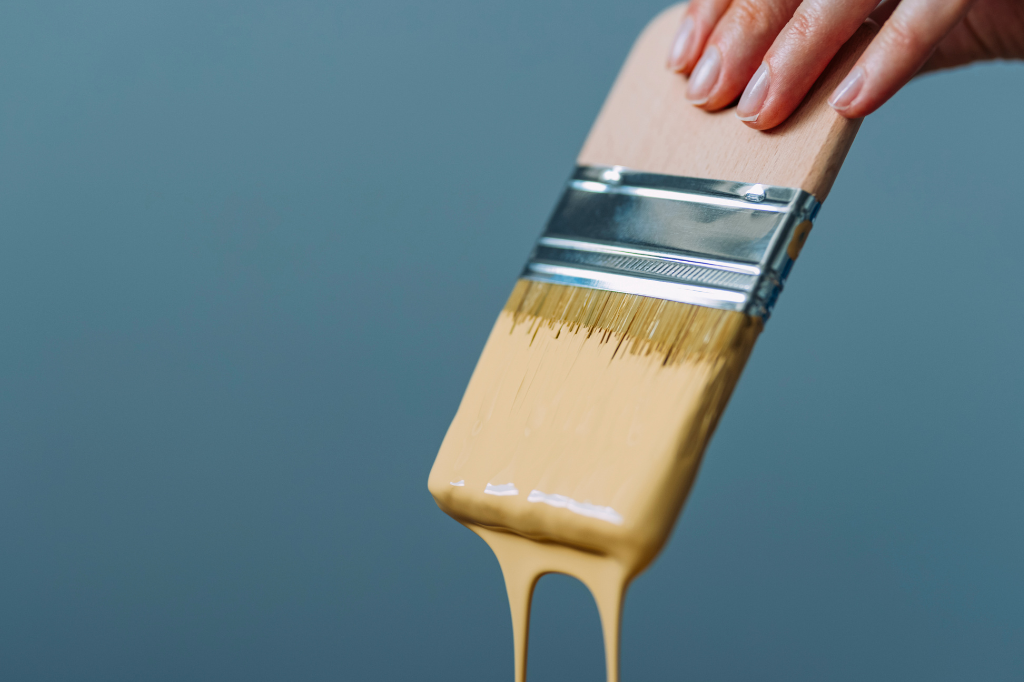 A person is pouring paint from a brush into a can.