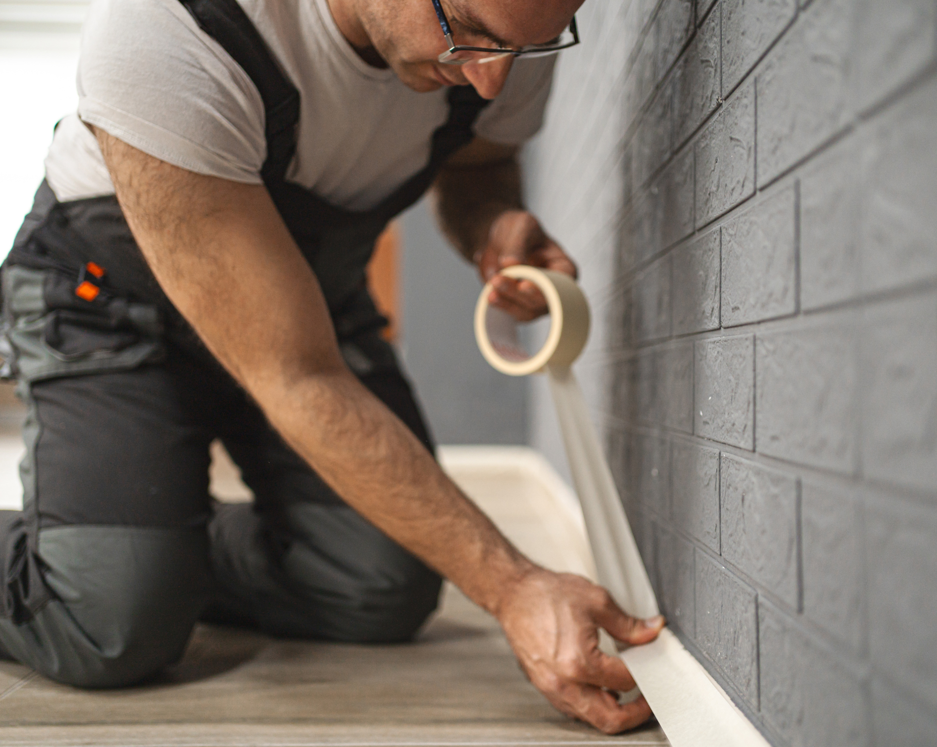 A man is kneeling down and applying tape to a wall.