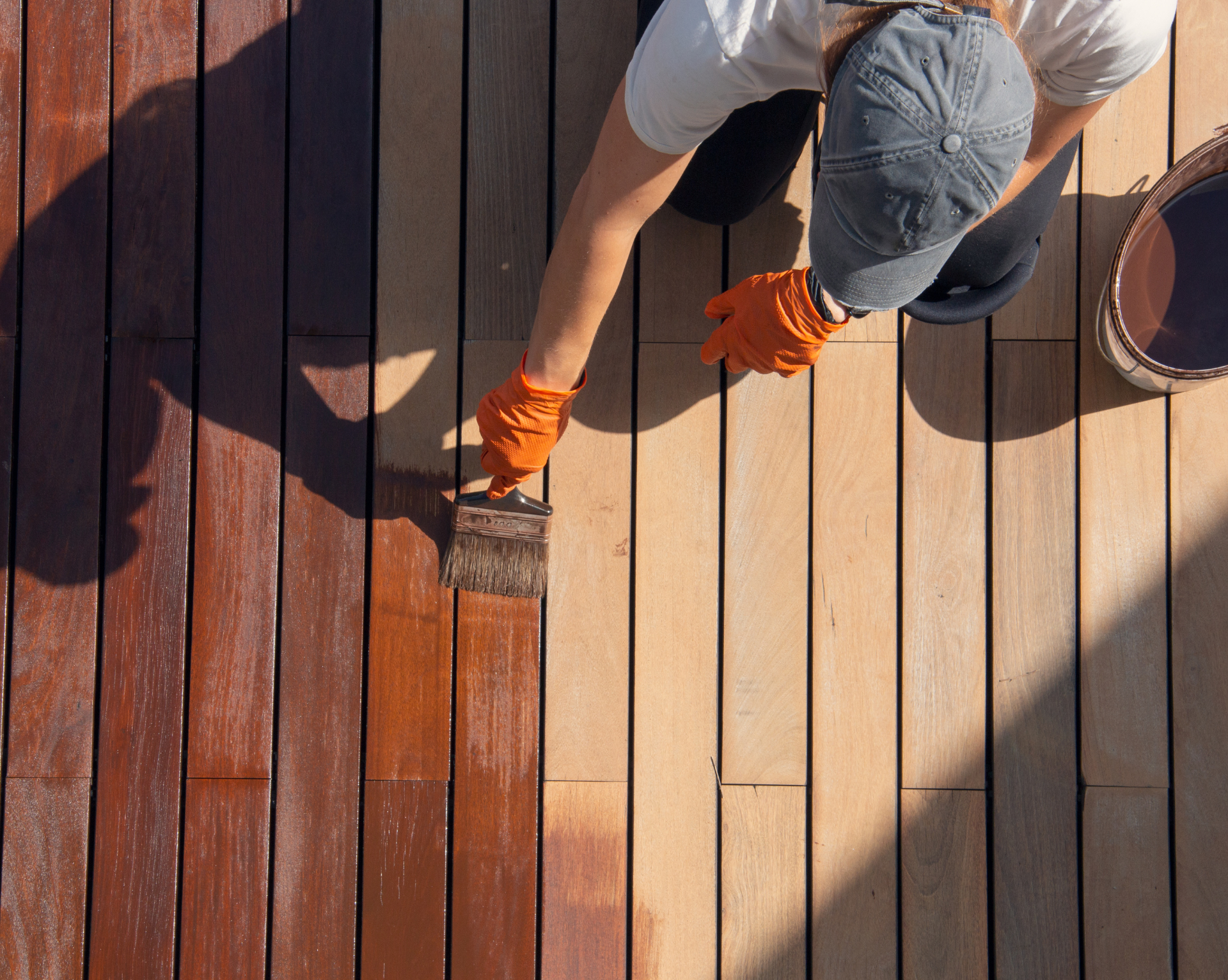 A man is painting a wooden deck with a brush.