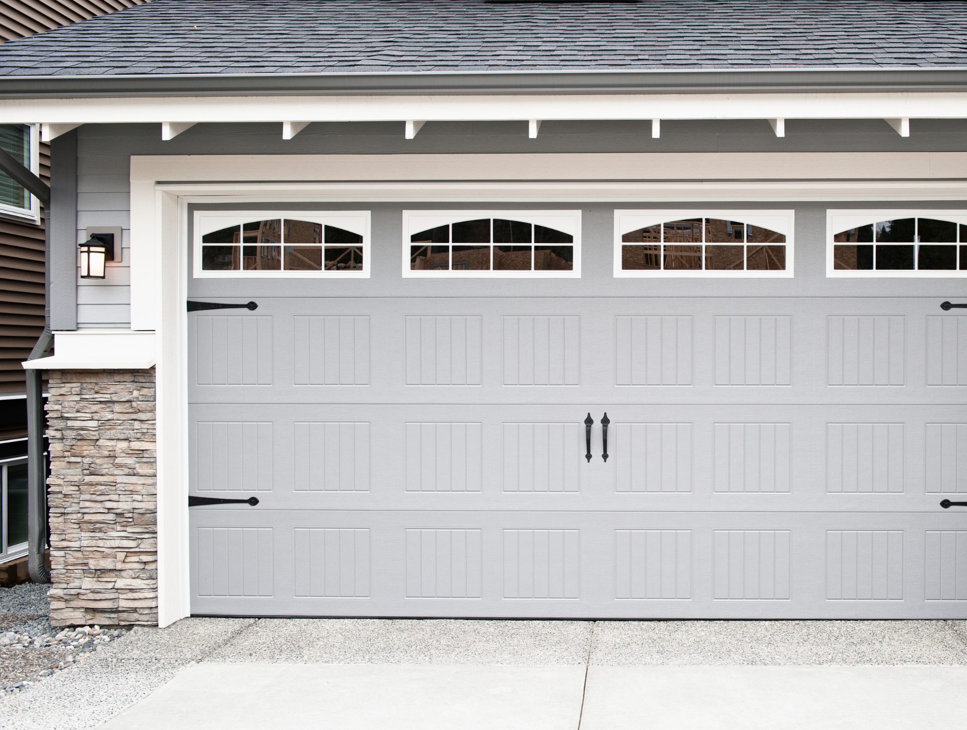 A gray garage door with a stone wall and a roof.