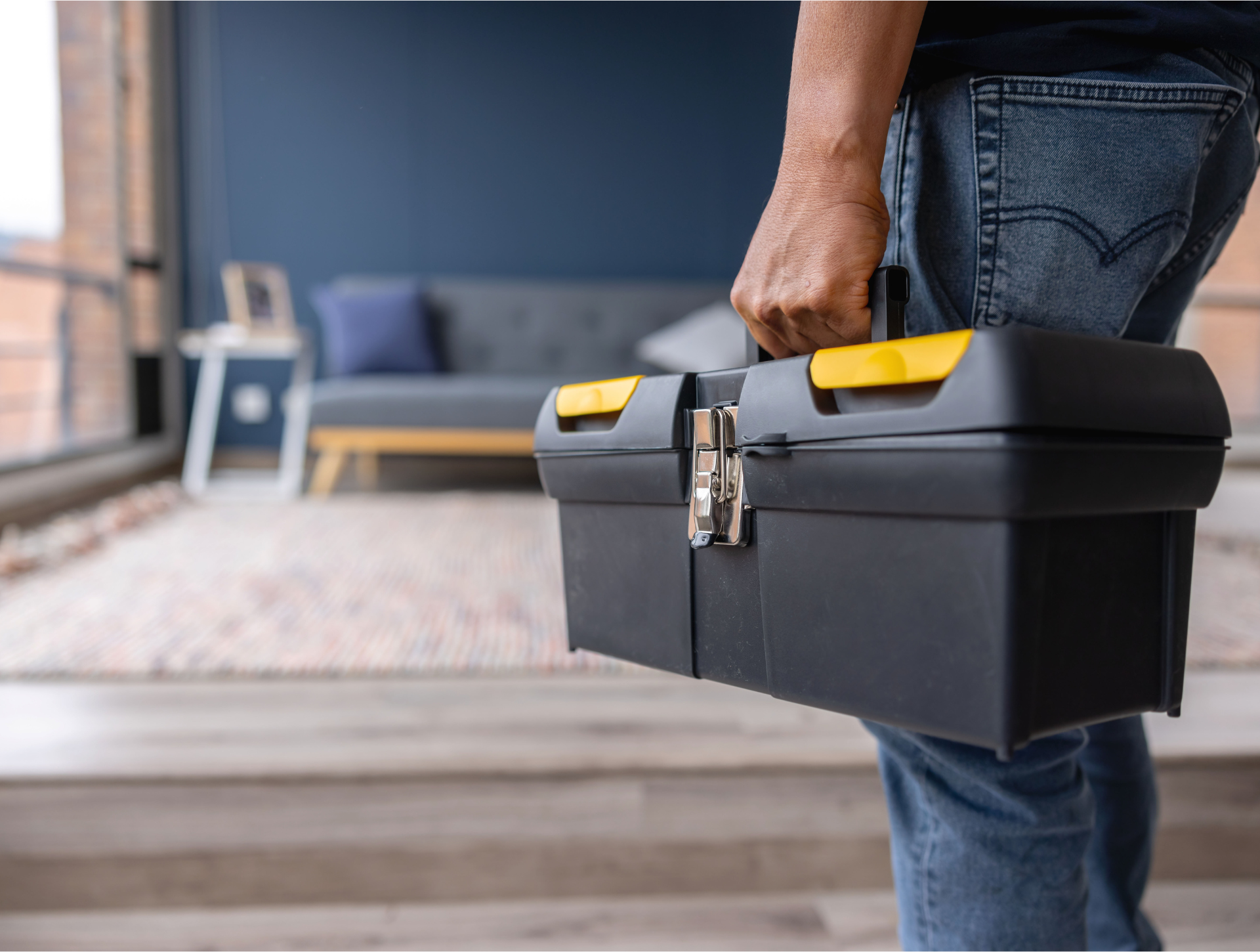 A man is carrying a toolbox in a living room.