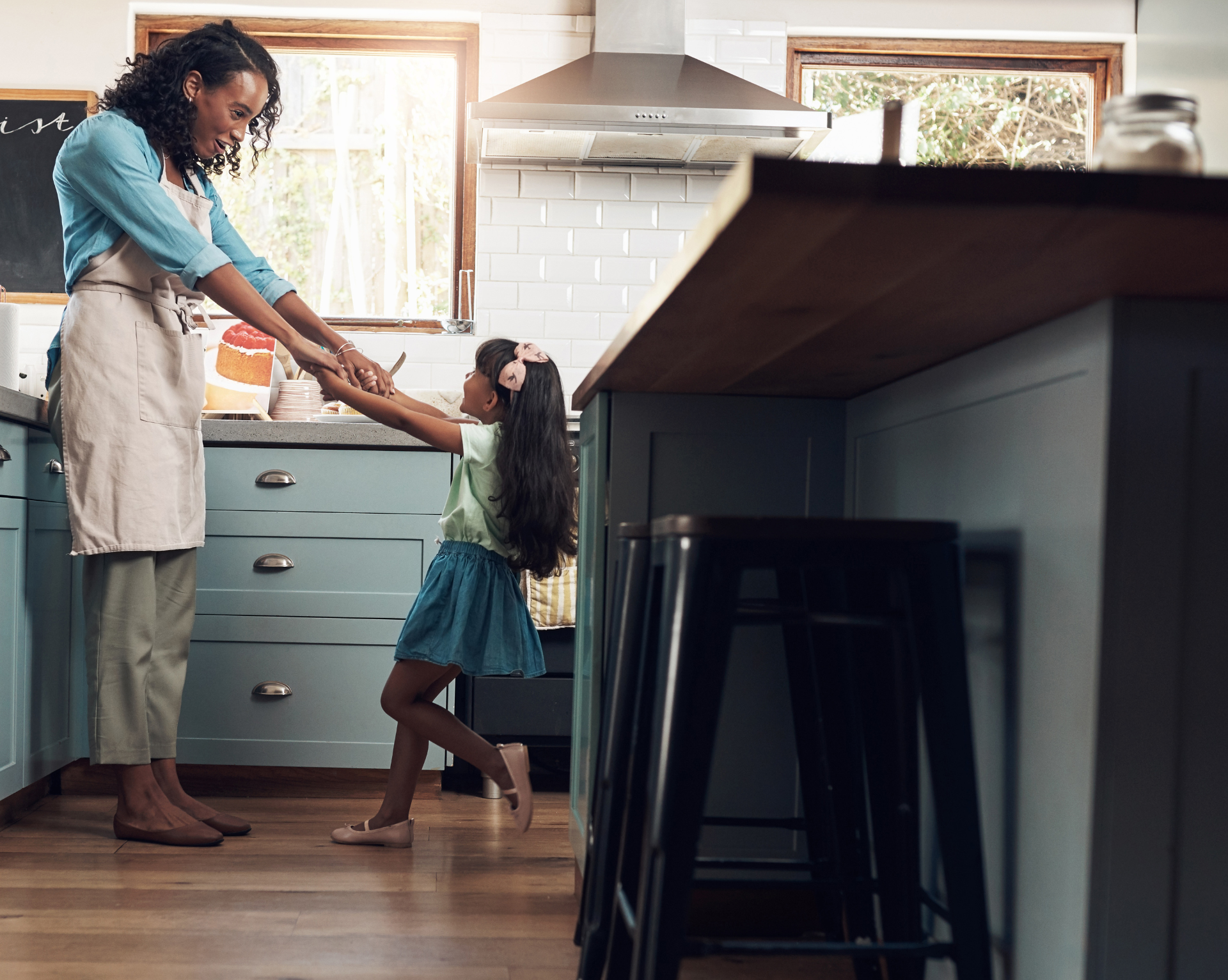 A woman and a little girl are dancing in a kitchen.