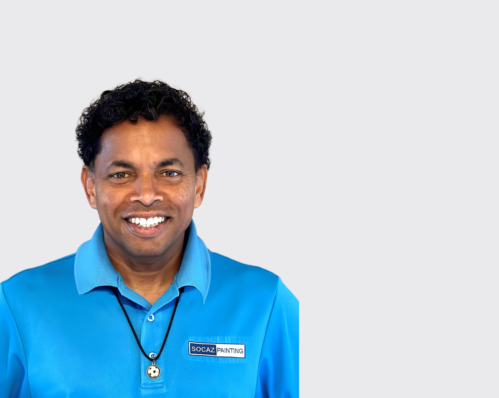 A man wearing a blue shirt and a necklace is smiling