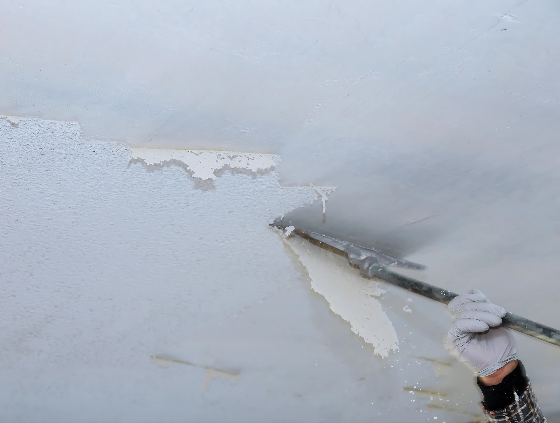 A person is peeling paint off of a wall with a spatula.