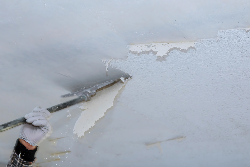 A person is peeling paint off of a wall with a spatula.